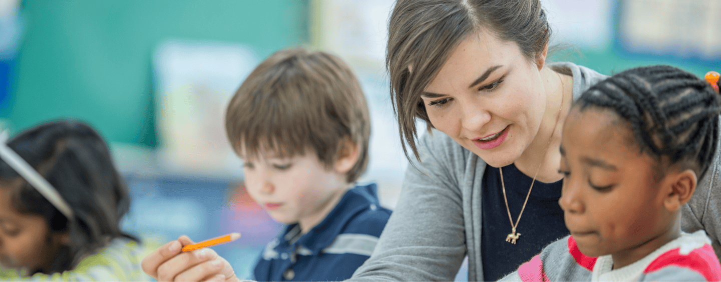 female teacher sitting at a table working with elementary students